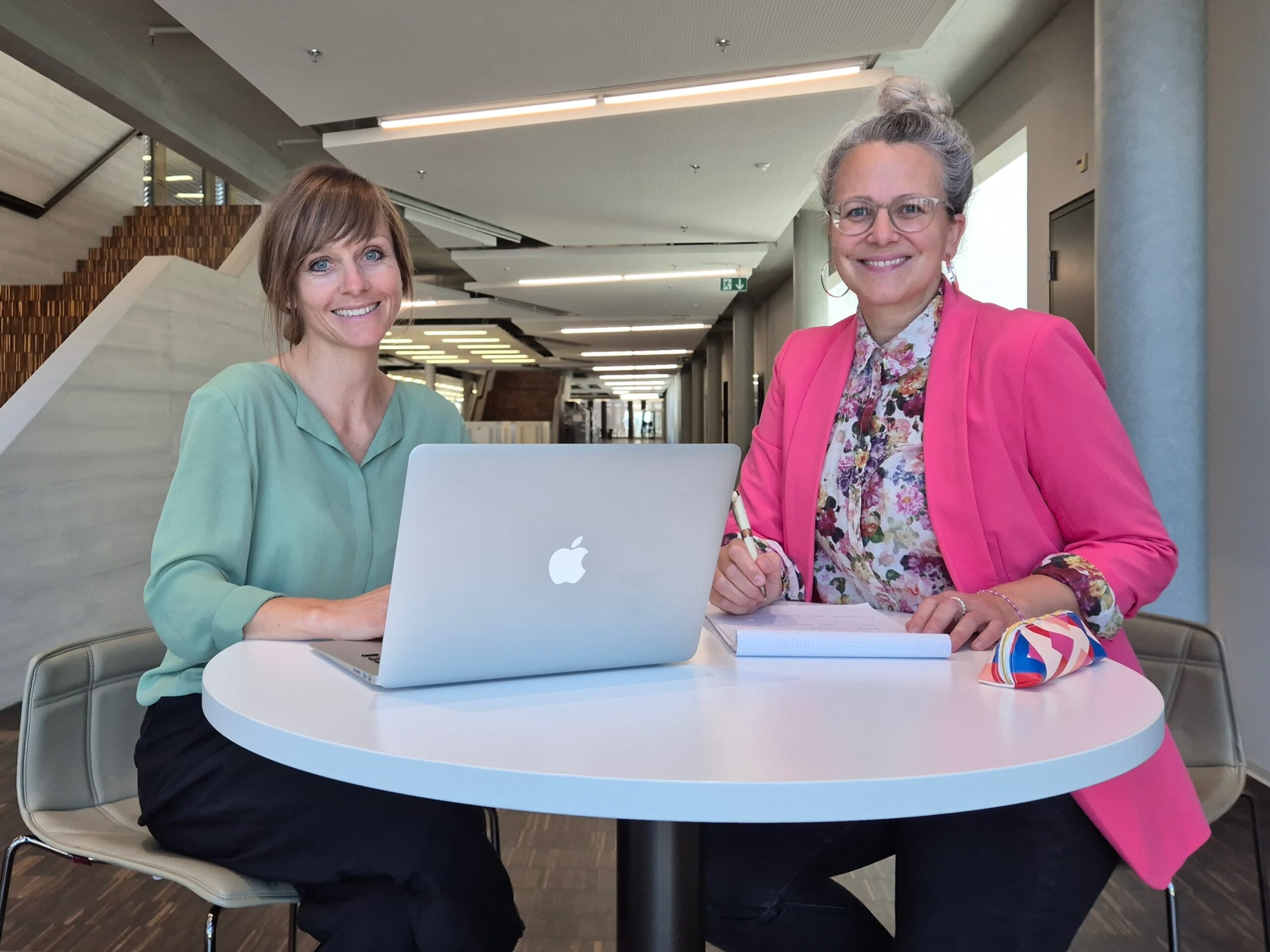 Maila Bermejo und Sabrina Müller von Projekt Lehre sitzen an einem Tisch mit Arbeitsmaterialien vor sich
